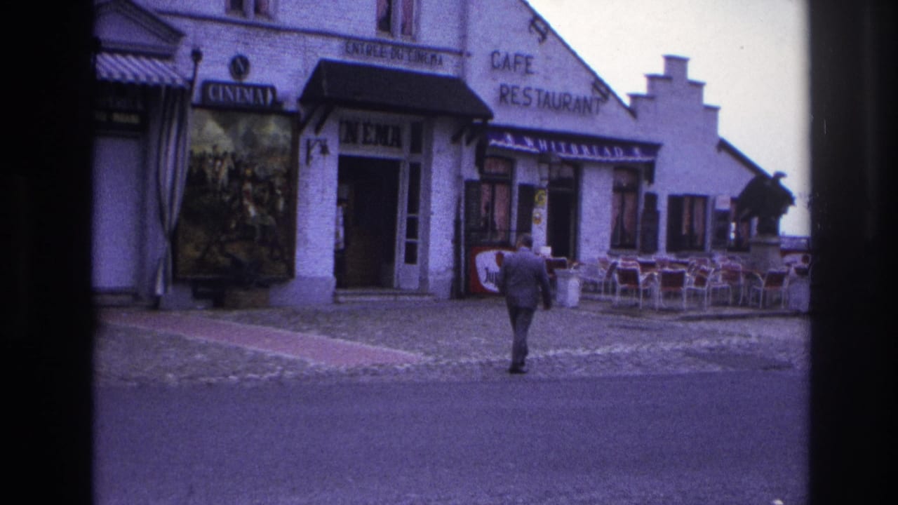 1967 Paris street view of a suited man approaching a cinema and cafe restaurant facade with posters and outdoor seating.