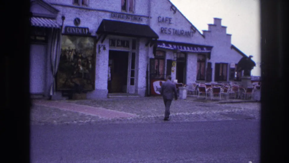 1967 Paris street view of a suited man approaching a cinema and cafe restaurant facade with posters and outdoor seating.