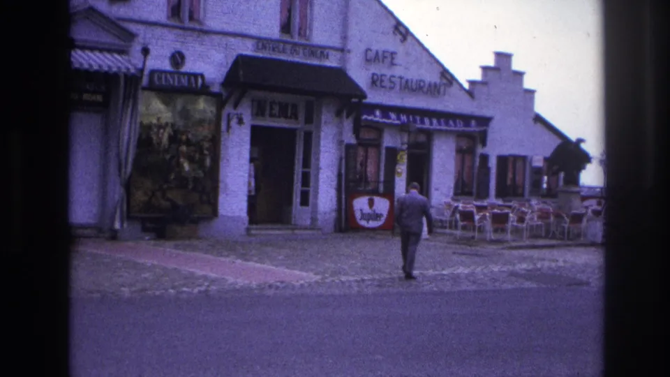 1967 Paris cinema and cafe exterior with a suited pedestrian, outdoor seating, and visible Jupiler beer advertising.