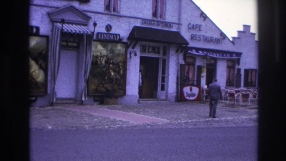 1967 Paris street footage showing a man walking away from camera near a cinema entrance, large poster, and cafe chairs.
