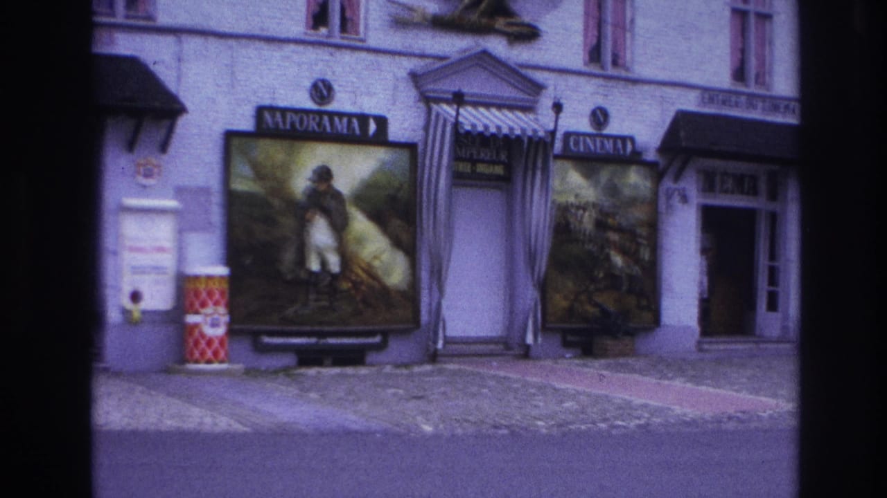 1967 Paris 8mm frame showing a Naporama facade with painted posters, cinema signage, striped entrance awning, eagle sculpture, and street barrels.