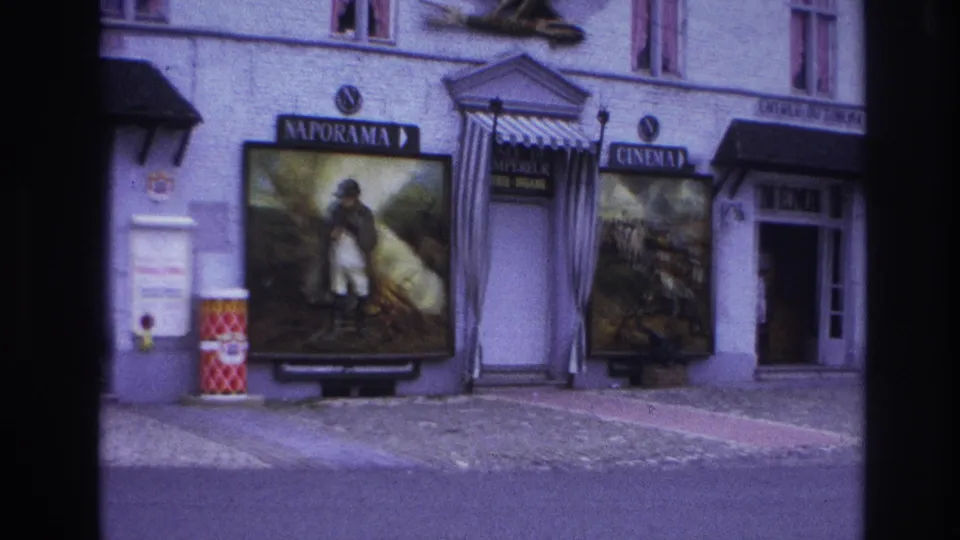 1967 Paris 8mm frame showing a Naporama facade with painted posters, cinema signage, striped entrance awning, eagle sculpture, and street barrels.