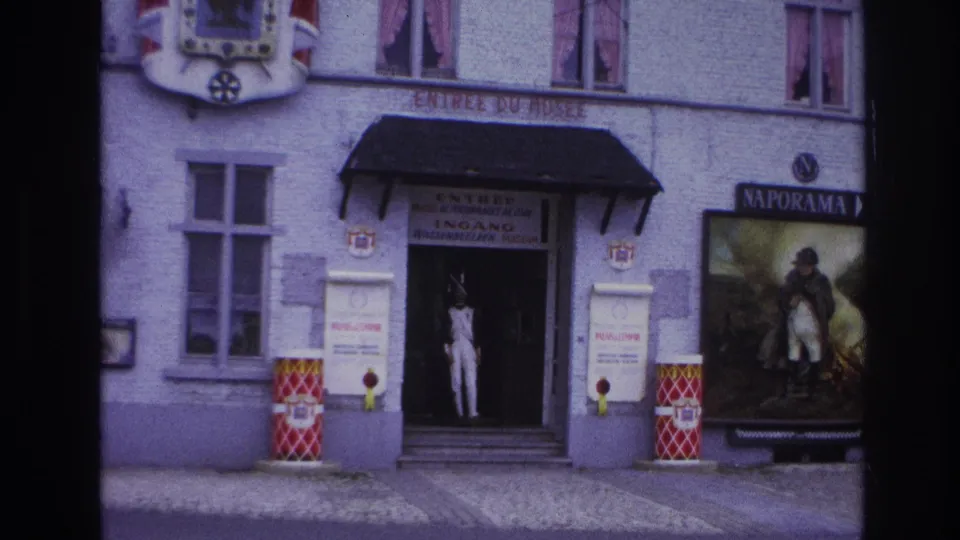 1967 Paris frame centered on the museum entrance, with a white-uniformed mannequin in the doorway and a Naporama Napoleon poster to the side.