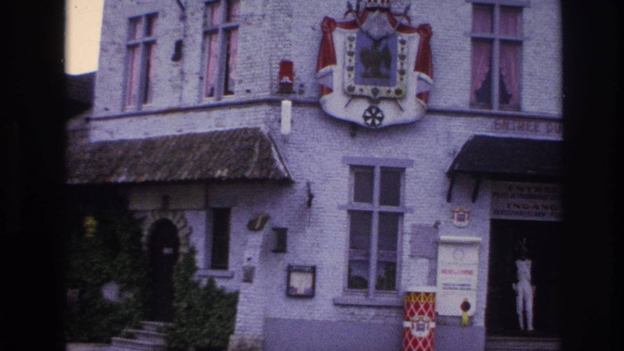 1967 Paris 8mm frame showing a white masonry building with heraldic shield, ivy, signage, and a person standing in the entrance.