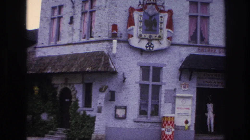 1967 Paris 8mm frame showing a white masonry building with heraldic shield, ivy, signage, and a person standing in the entrance.