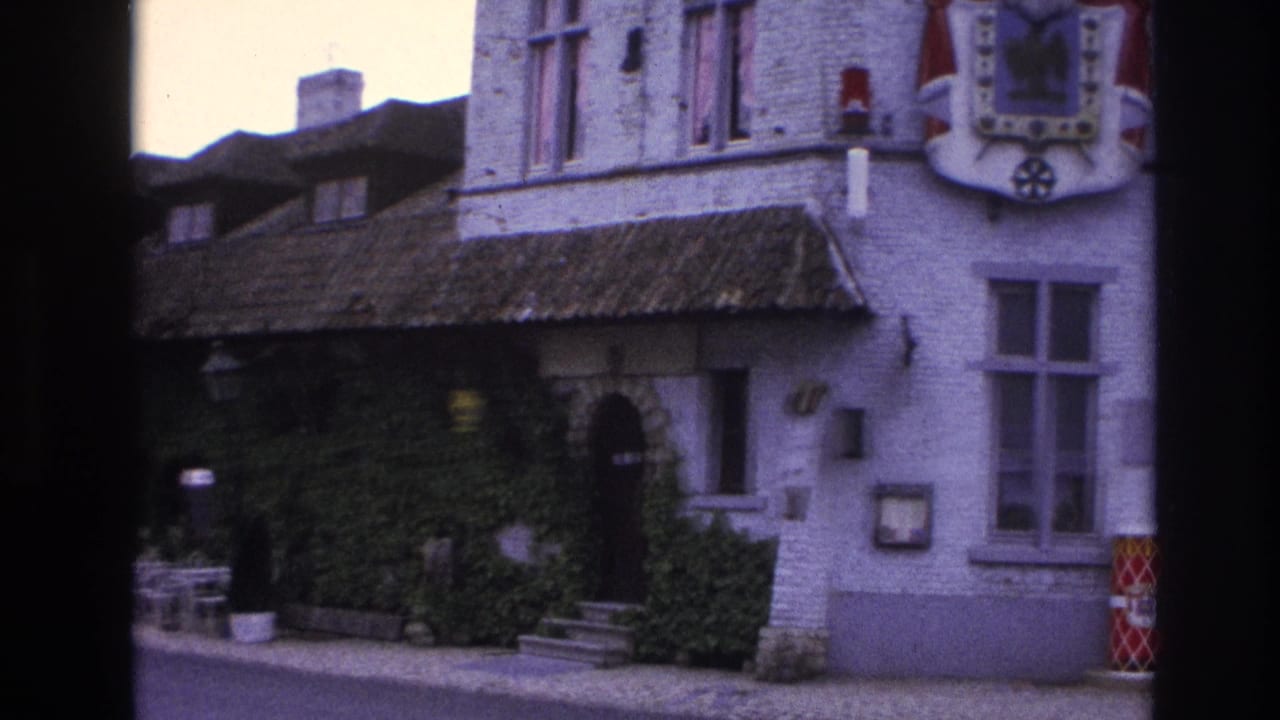 1967 Paris 8mm frame with an ivy-covered building front, tiled roof edge, outdoor seating, and a partial heraldic shield on the upper wall.