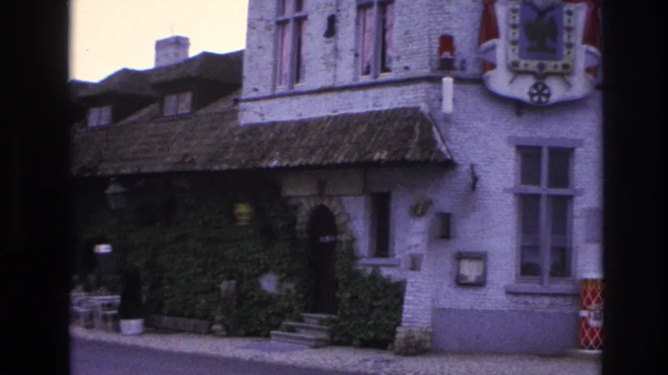 1967 Paris 8mm frame with an ivy-covered building front, tiled roof edge, outdoor seating, and a partial heraldic shield on the upper wall.