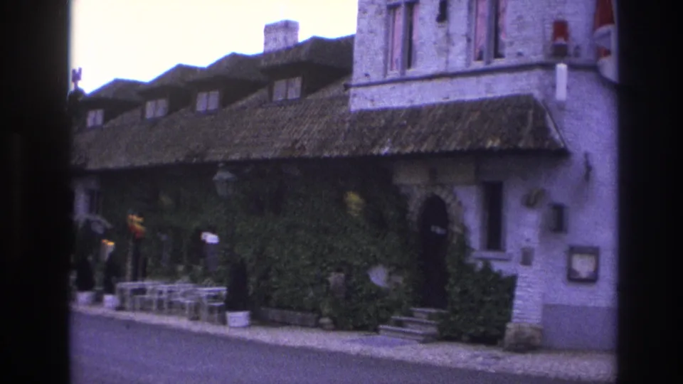 1967 Paris 8mm frame showing a panning view across outdoor chairs, people at the edge of frame, ivy, and a historic-style doorway.