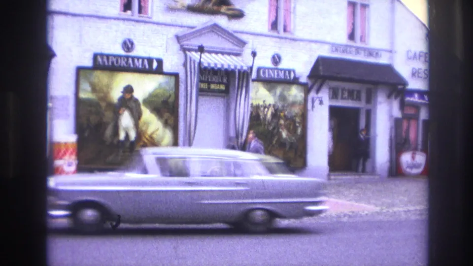 1967 Paris street frame showing a cinema entrance, large Napoleonic-themed posters, signs, and a blurred passing car.