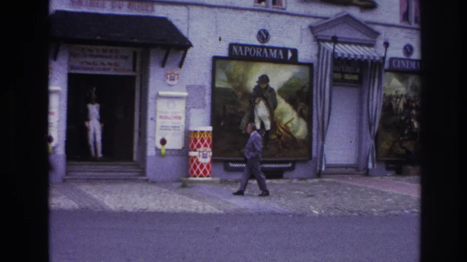 A 1967 Paris street frame shows a suited man near a doorway display and large Napoleonic-themed poster.