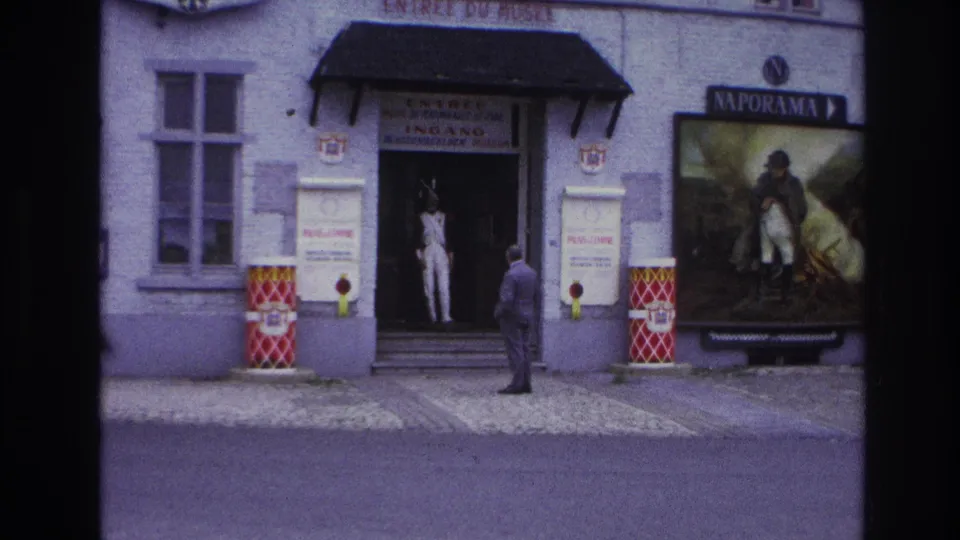 Paris museum frontage with a man paused near the entrance, a white mannequin in the doorway, and a large Naporama display poster.