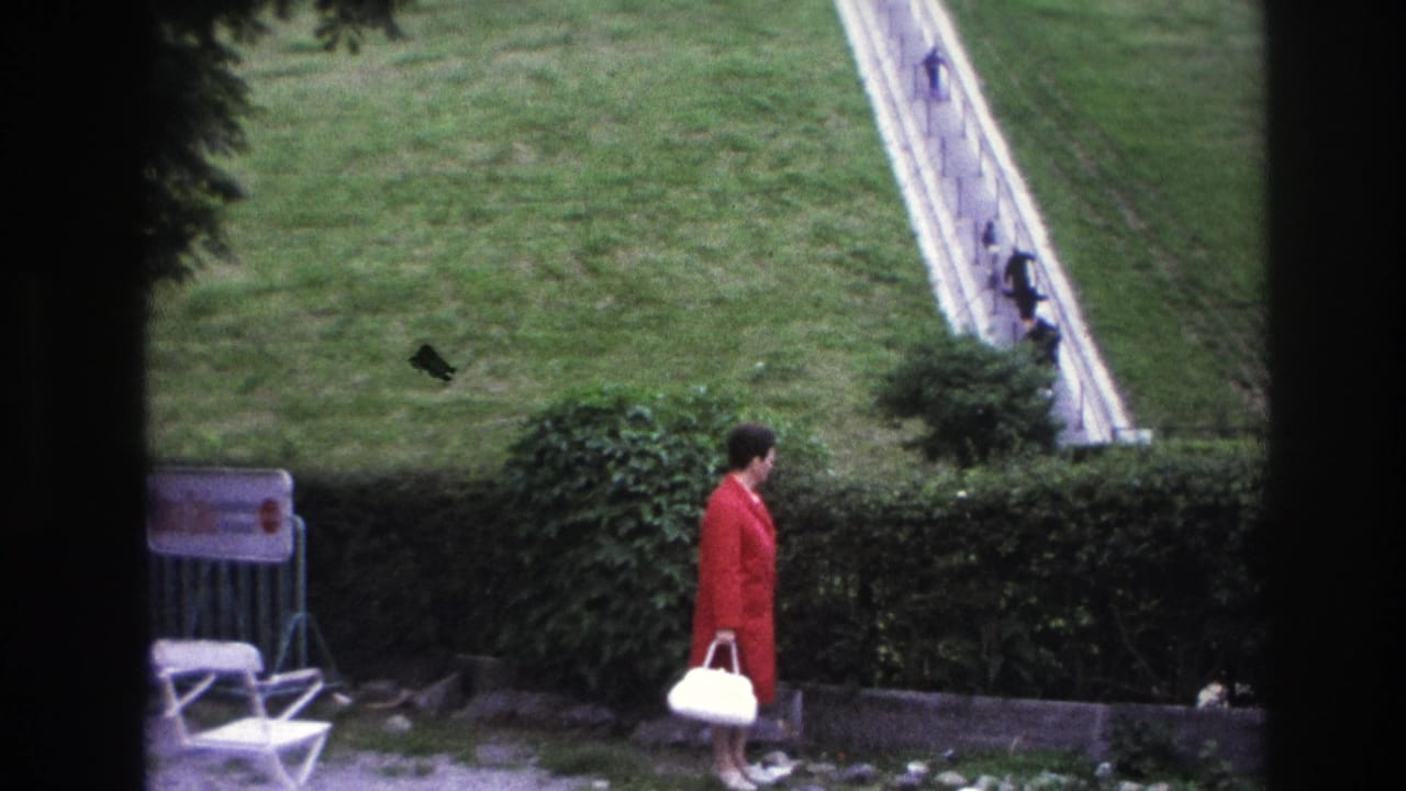 1967 Paris 8mm frame showing a woman with a white handbag watching distant pedestrians climb a steep white stairway across a grassy hill.