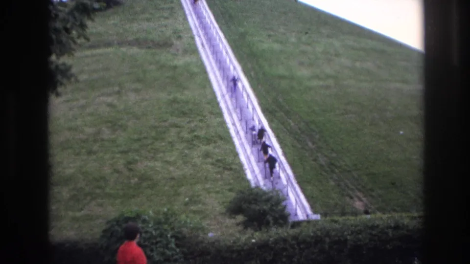 Final 1967 Paris frame with the woman partly visible below, distant climbers on the steep stairway, and dark window-like borders around the view.