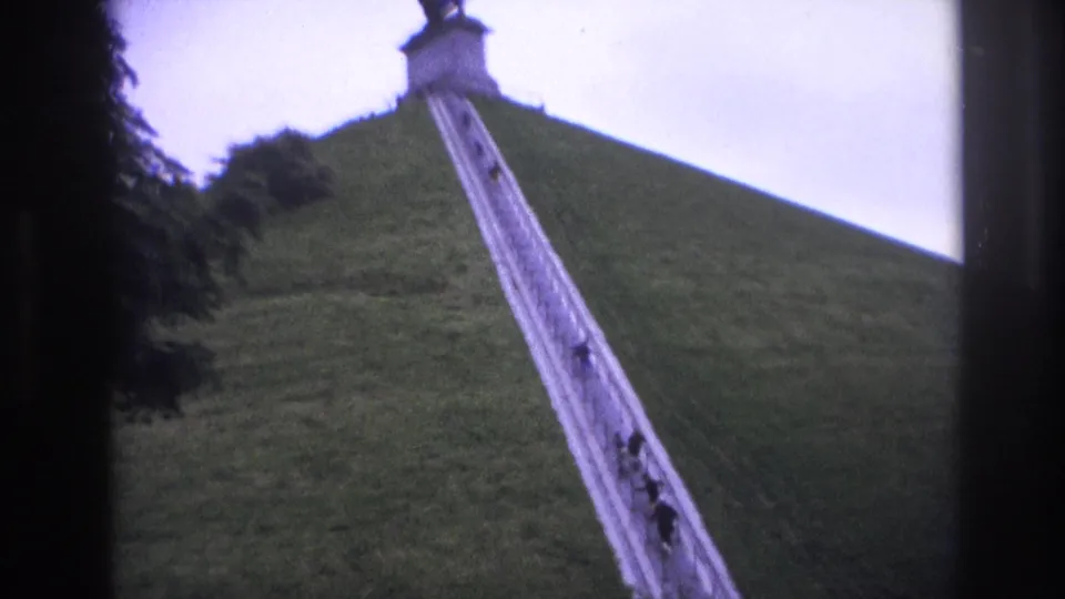 The stairway leads up the grassy mound toward the silhouetted lion statue and monument, with visitors visible on the steps.