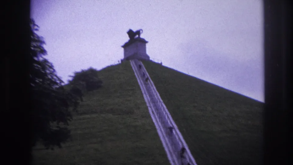 A handheld 8mm frame shows the stairway cutting up the grassy mound toward the lion-topped monument, with visitors spaced along the climb.