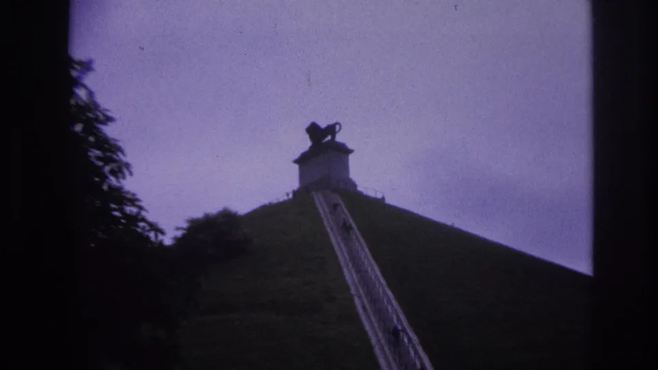1967 Paris home-movie frame showing distant visitors climbing a steep hillside stairway toward a silhouetted lion statue.
