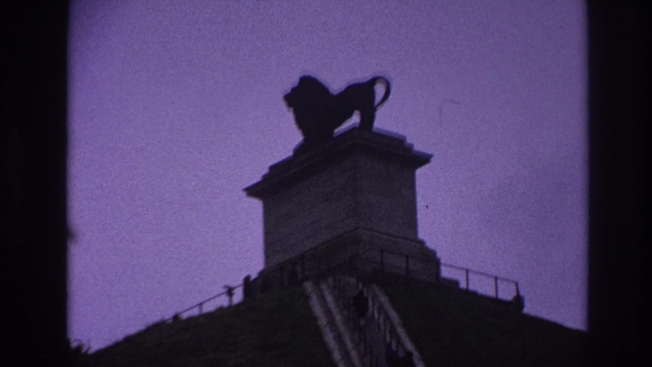 1967 Paris home-movie frame showing a silhouetted lion statue atop a stone pedestal, with railing and monument edges below.