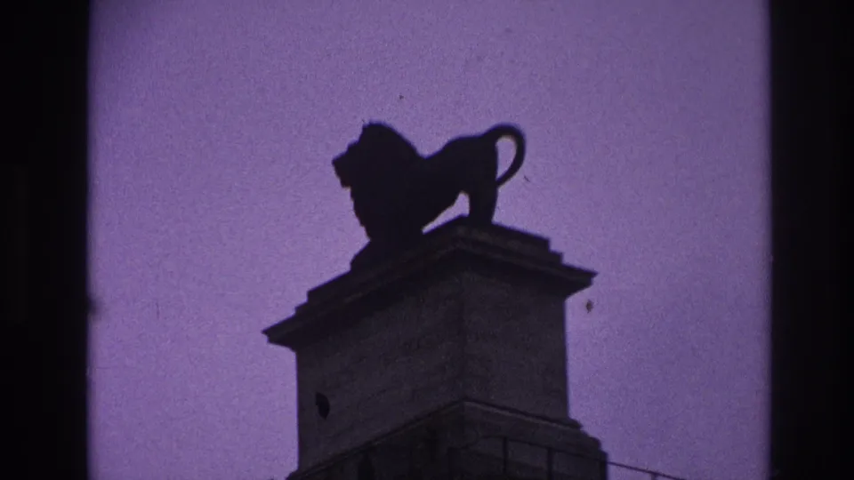 1967 Paris frame showing the lion statue and pedestal from below, with dark film edges and a tinted sky.