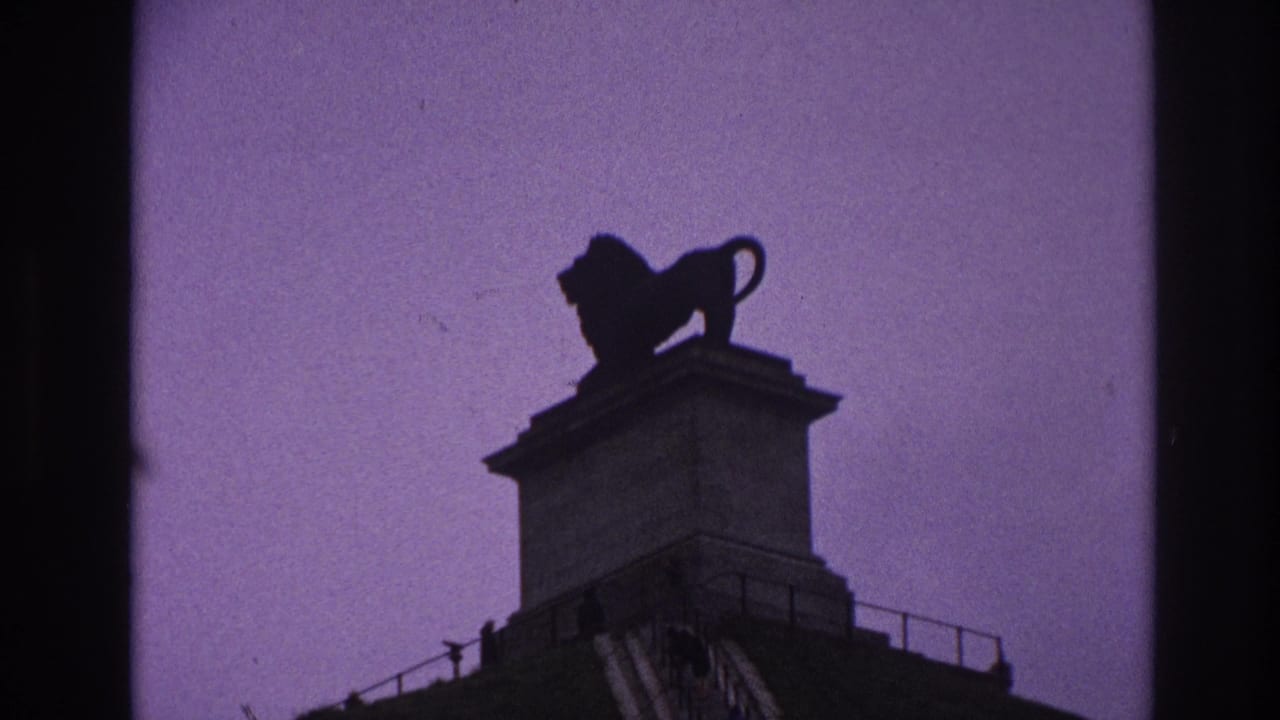 1967 Paris 8mm frame showing a dark lion statue on a stone pedestal against a purple dusk sky.