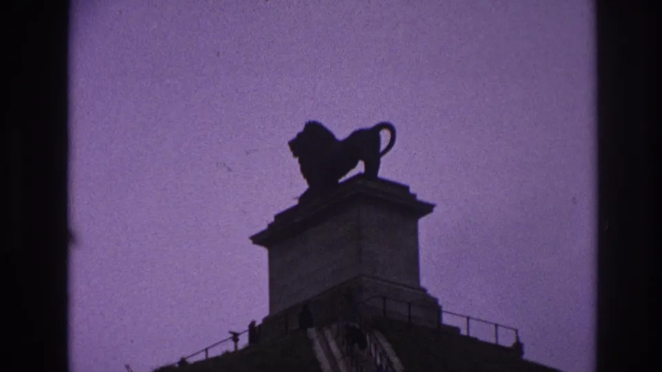 1967 Paris 8mm frame showing a dark lion statue on a stone pedestal against a purple dusk sky.