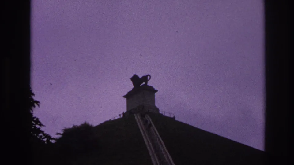 Wider 1967 Paris 8mm frame with the lion monument above a steep staircase and dark trees at the edge.