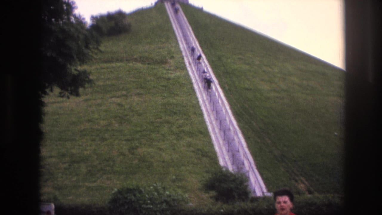 1967 Paris home-movie frame showing a steep grassy slope with a long white staircase and small figures ascending near the top.
