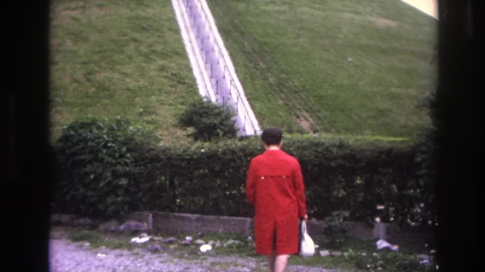 1967 Paris frame showing the woman from behind, carrying a white handbag near the hedge below the steep hillside stairs.
