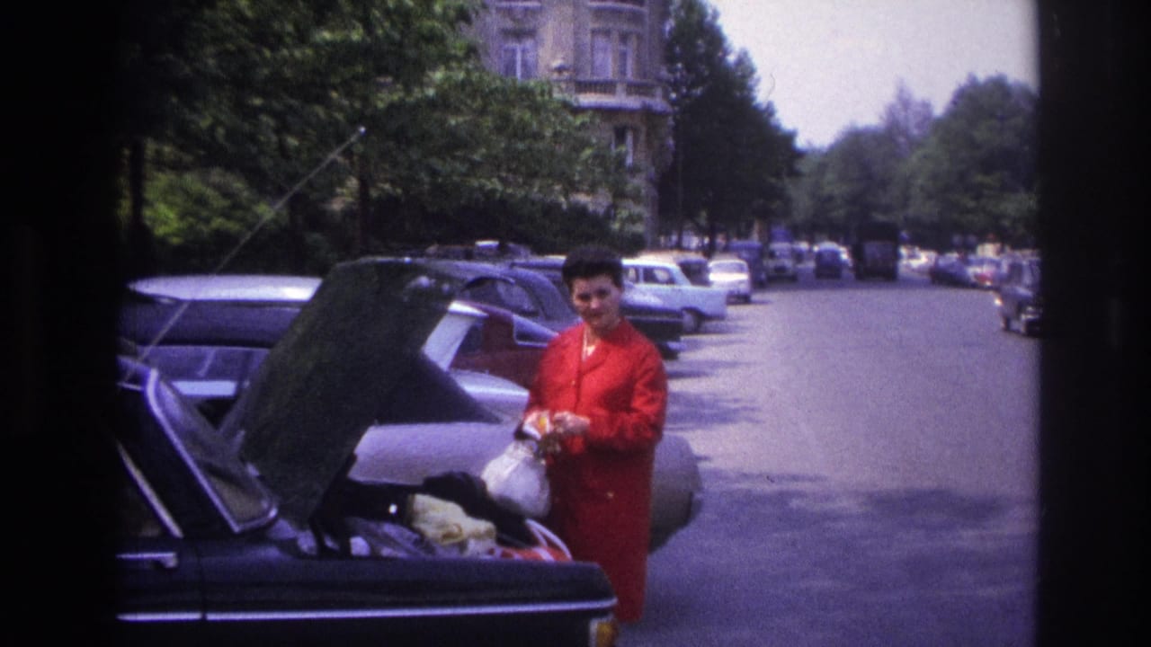 In 1967 Paris footage, a woman in red stands next to an open car trunk on a street lined with parked cars.