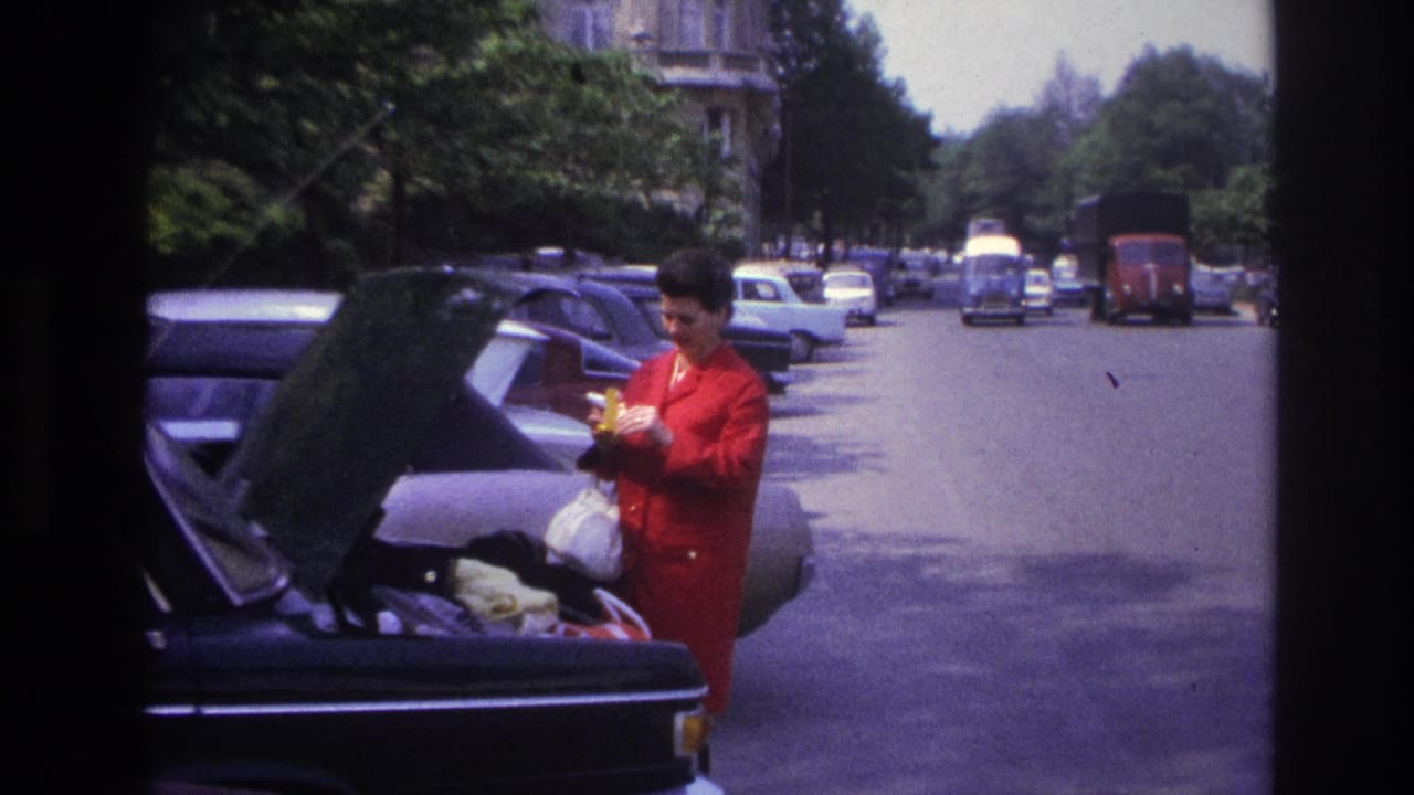 Woman looks down while holding small items beside an open car boot.