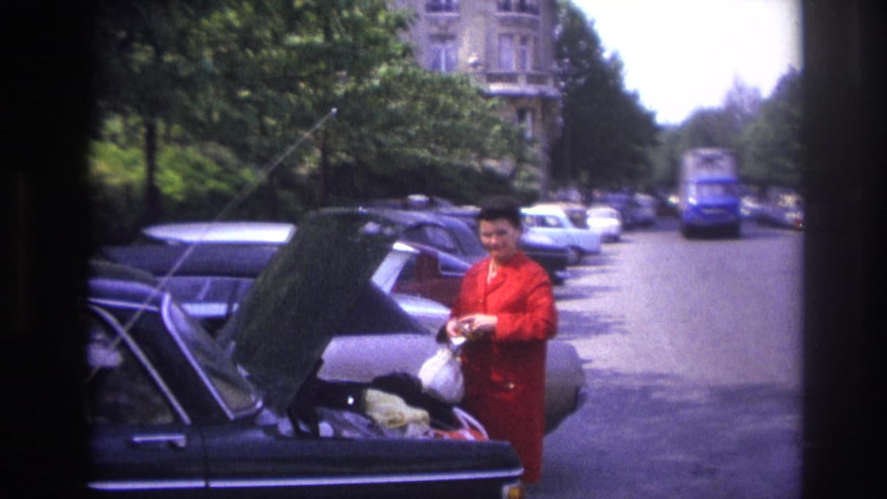 1967 Paris street frame with a woman in red beside a parked car trunk, traffic and a blue truck visible in the background.