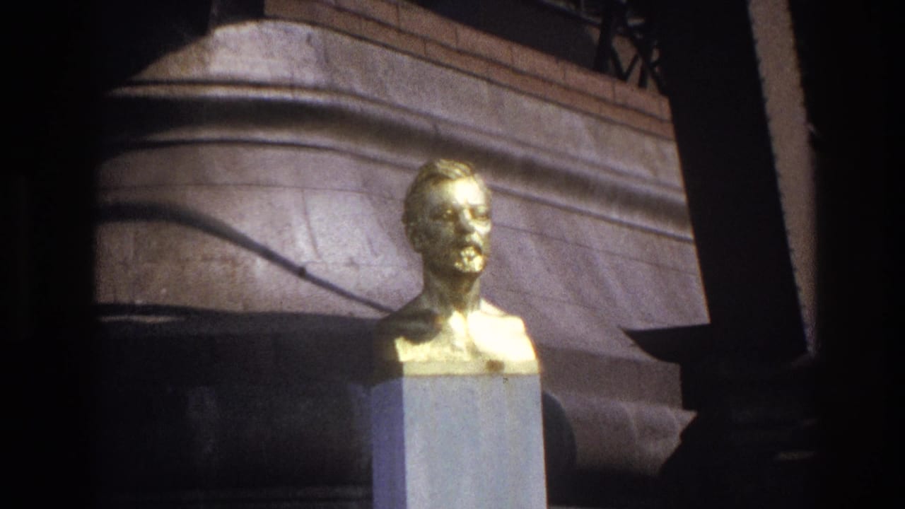 Gilded bust on pedestal with stone wall, railing, and dark frame edge.