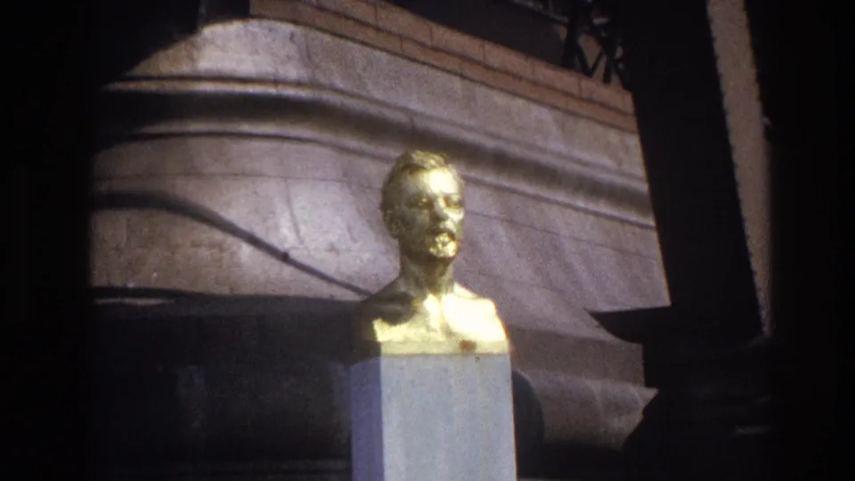 1967 Paris frame with the gilded bust slightly farther back, set before stone architecture and partial railing.