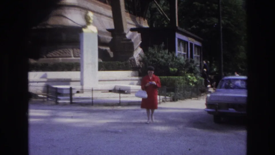 1967 Paris frame showing the woman in red facing the camera near the monument, with Eiffel Tower supports and a car visible.