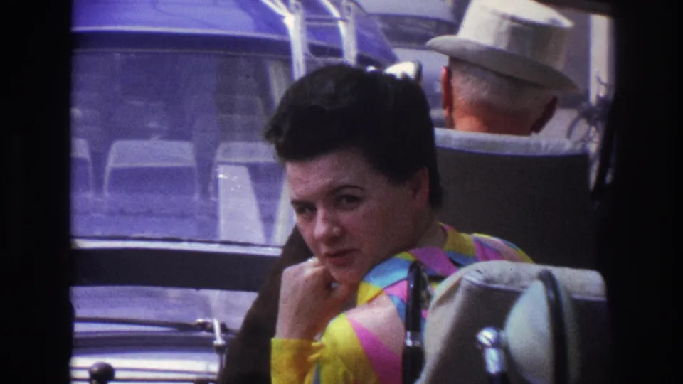 1967 Paris transit frame showing the seated woman looking toward the camera, framed by vehicle seats, windows, and a man in a light hat.
