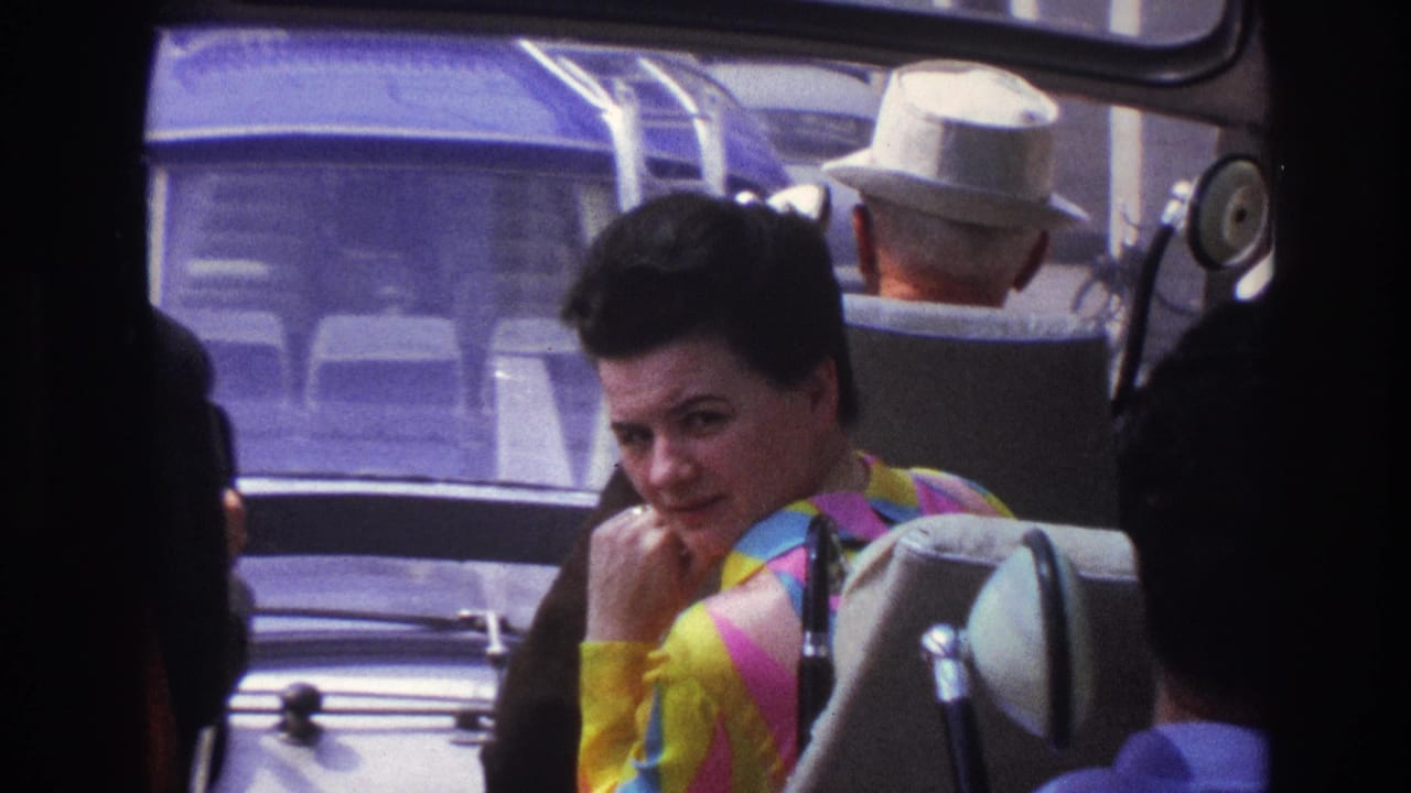 1967 Paris tour-bus passengers seen from inside the coach, with a woman in a bright striped top near the camera.