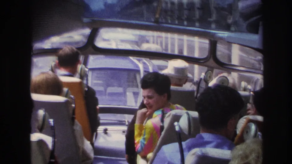 1967 Paris home-movie view from a tour bus, showing seated passengers and street traffic through the front windows.