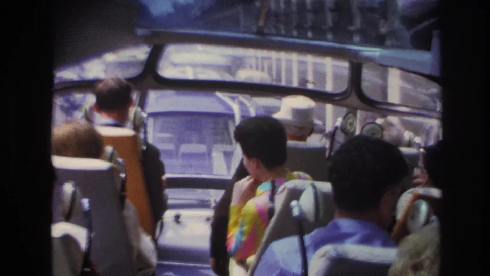 End frame of a 1967 Paris tour-bus ride, with passengers facing forward and the city visible through broad windows.