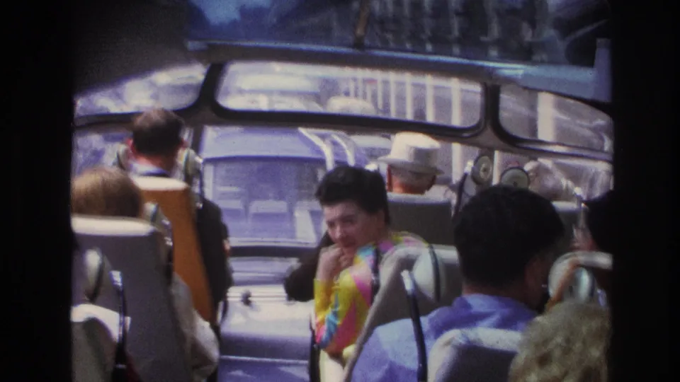 1967 Paris bus interior with adult passengers seated and a woman in a bright patterned dress smiling toward the camera.