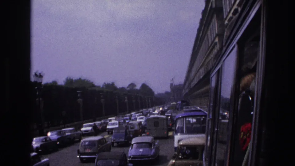 Paris street traffic in 1967 viewed from a bus window, with classic cars and vans moving under hazy daylight.