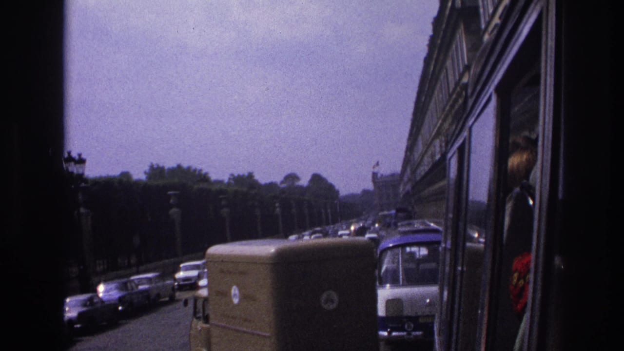 Traffic queue with cars, a van, a bus front, trees, and a reflected passenger near the window.