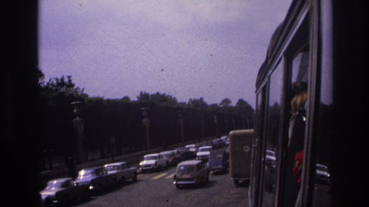 1967 Paris traffic with classic cars on a boulevard, framed by the dark interior edge of a moving vehicle.