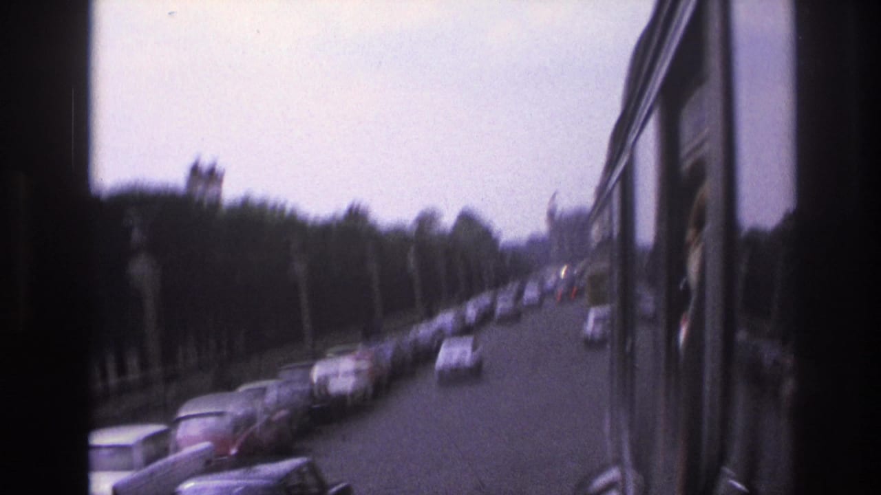 1967 Paris street traffic viewed from a moving vehicle, with parked cars, trees, and dark window framing.