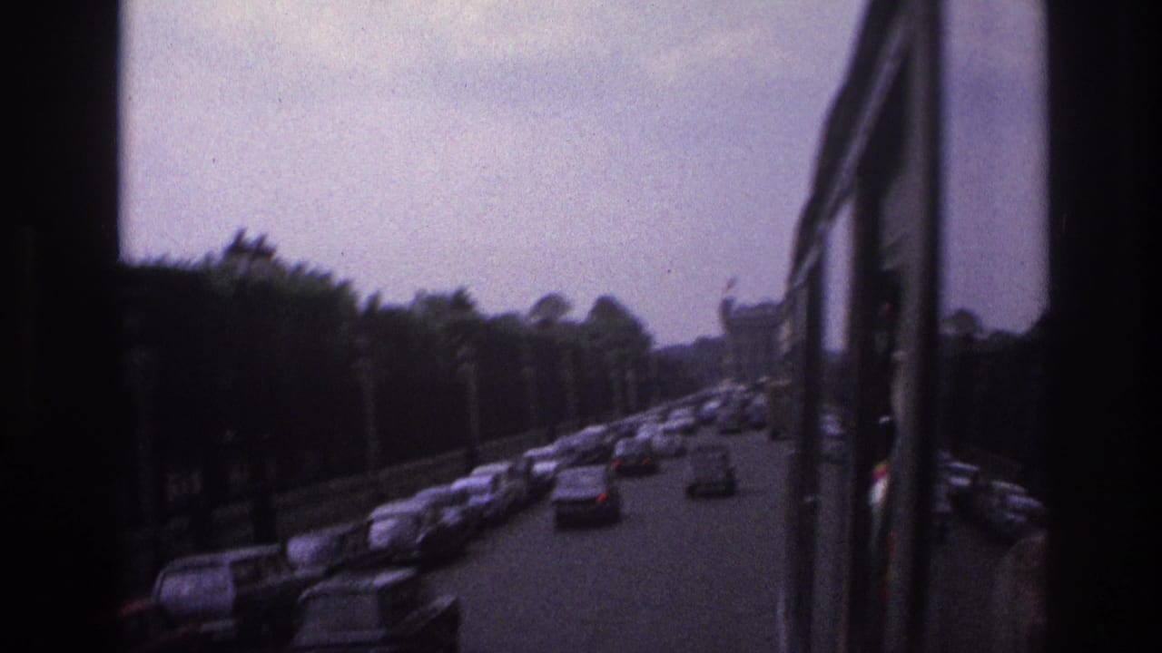 Bus-window view of 1967 Paris traffic on a broad tree-lined boulevard under a dim overcast sky.