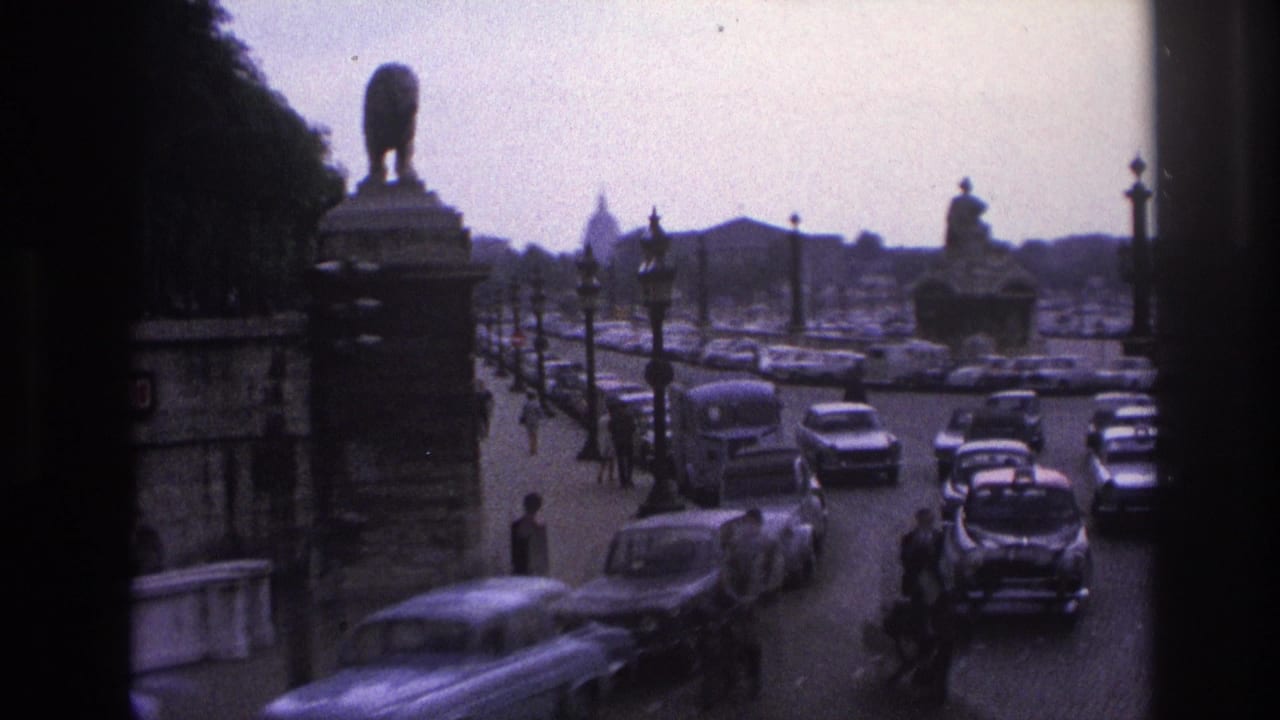 Traffic passes near a riverside road with monuments, lamps, and a distant dome.