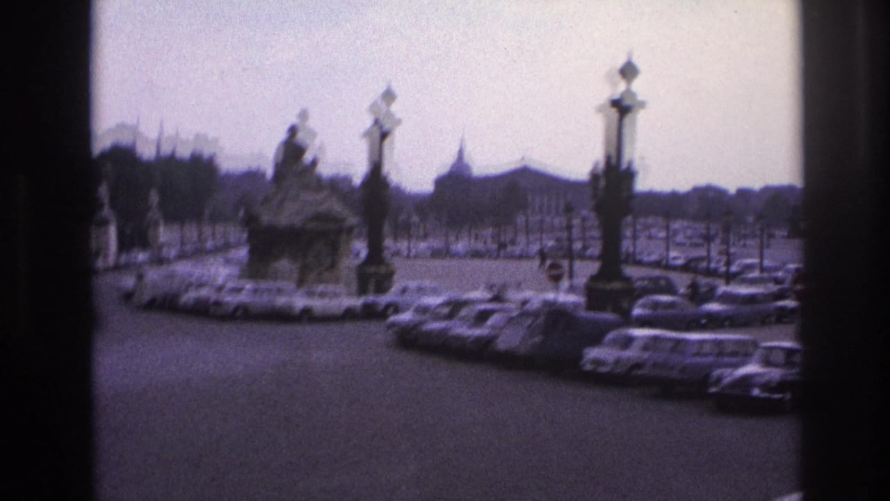 1967 Paris home-movie frame showing an ornate fountain, decorative lampposts, and parked cars viewed through a window frame.