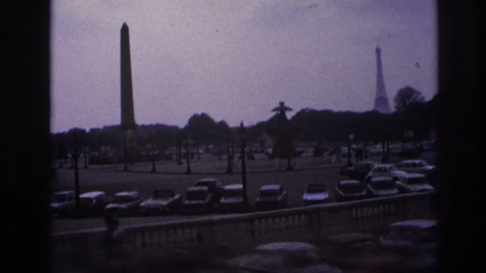 1967 Paris frame showing an obelisk, parked cars, and the Eiffel Tower in the distance under an overcast sky.