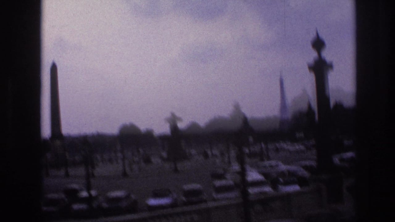1967 Paris home-movie view of cars around a traffic circle, framed by dark window edges, with an obelisk and Eiffel Tower visible in the distance.