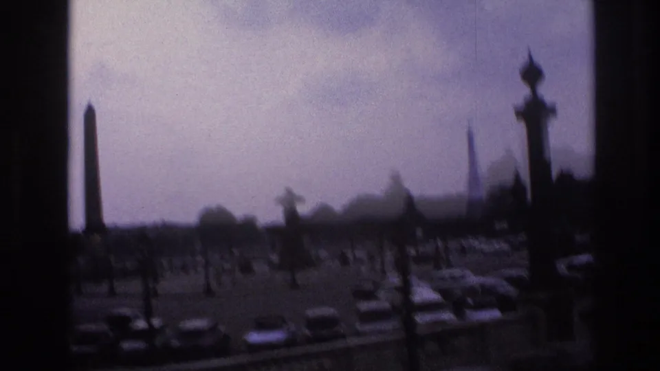 1967 Paris home-movie view of cars around a traffic circle, framed by dark window edges, with an obelisk and Eiffel Tower visible in the distance.