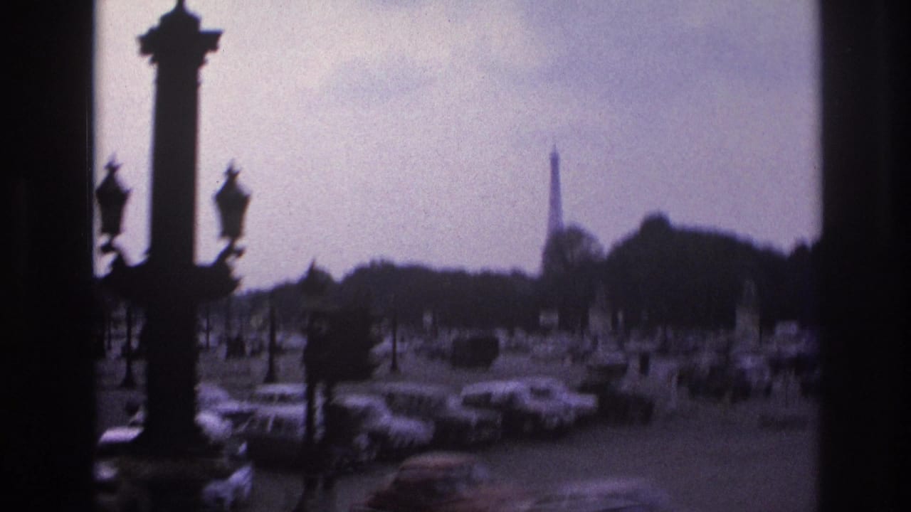 Monument columns and streetlamps overlook a busy roadway with the Eiffel Tower in the background.