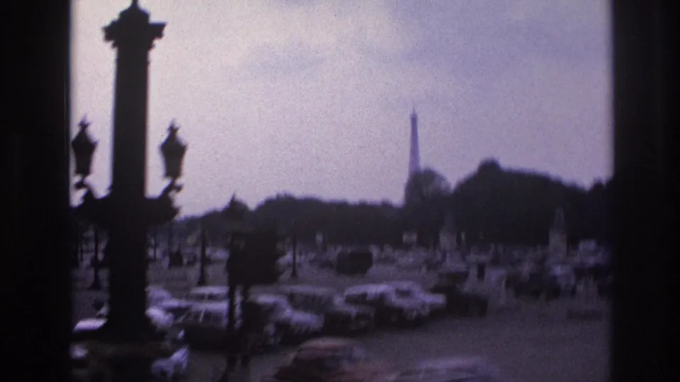 1967 Paris traffic scene with silhouetted monument columns, ornate lamps, cars below, and the Eiffel Tower beyond the trees.